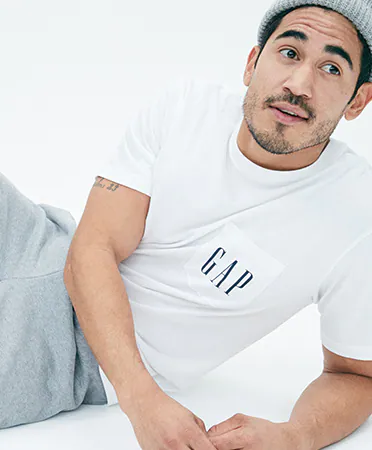 a man in a GAP tee shirt poses on the floor with jeans and a grey beanie