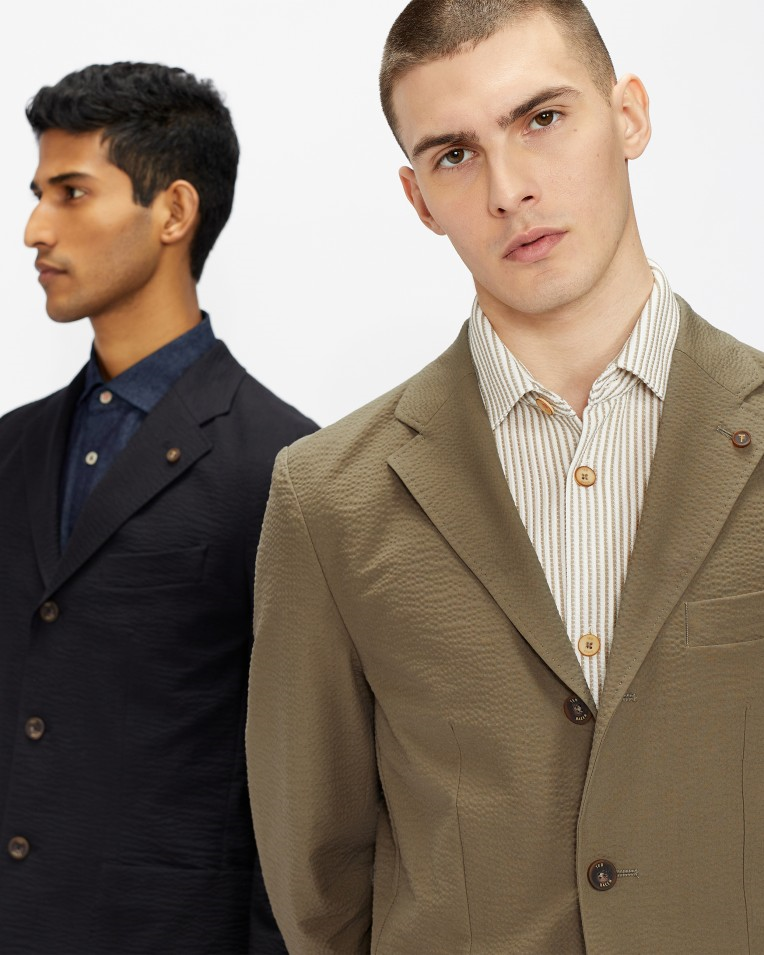 two men pose together in casual spring suits, one is tan and the other is navy