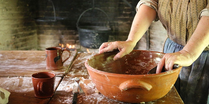 a woman in historic dress with historic cooking instruments stirs flour in a bowl