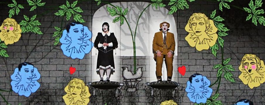 two actors on stage with a CGI background of vines, flowers, and animated faces