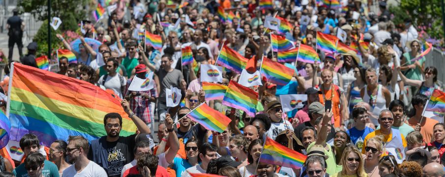 A large crowd of people march for Pride with rainbow flags