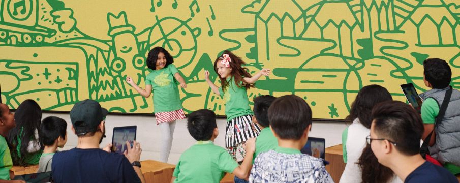 two children dance in front of a group of other children in apple branded tee shirts 