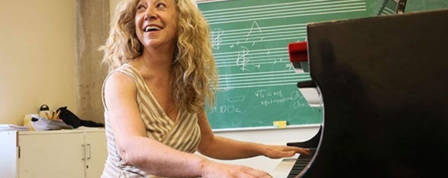 woman smiles while playing piano in a classroom