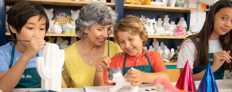 An older woman helps a young boy paint a piece of pottery at a color me mine studio