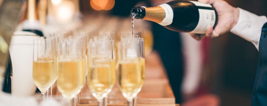 a waiter pours champagne into a row of glasses on a wooden bar top