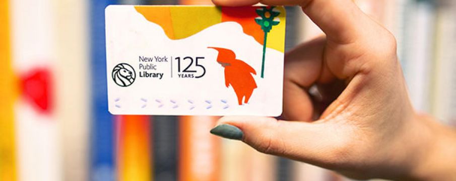 a hand with blue painted nails holds up a special edition library card for the 125th anniversary of the new york public library