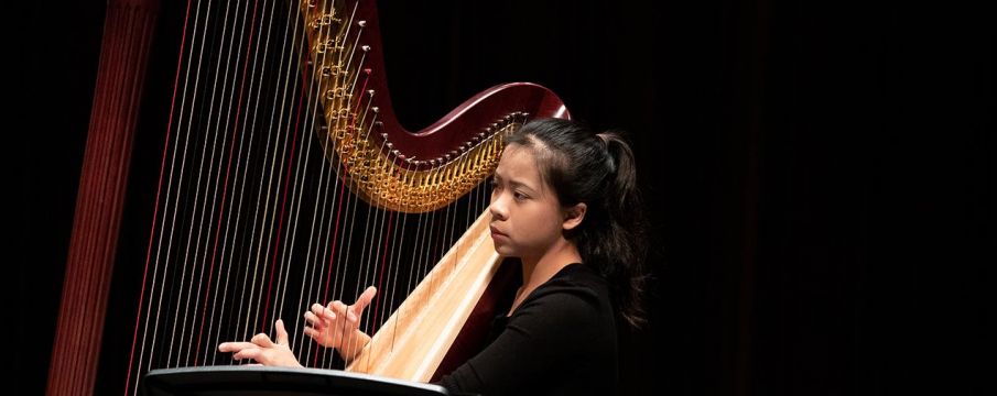 Juilliard musician plays the harp against a black background