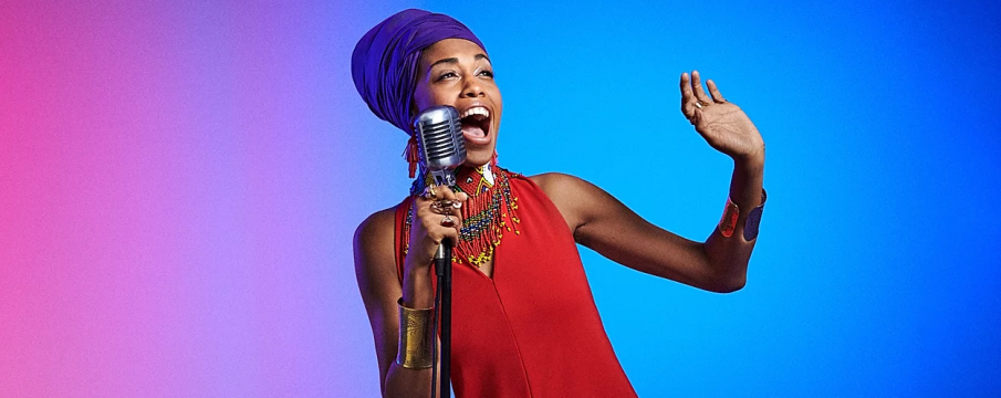 Jazzmeia Horn sings into a mic with a blue and purple background