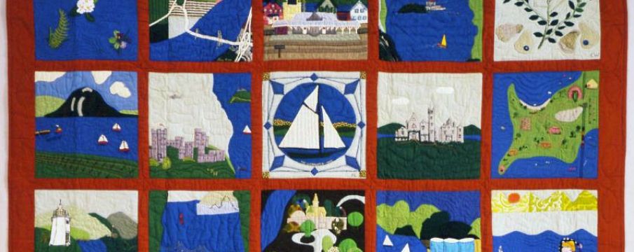 a quilt with mostly blue, greeb, and red fabric, with each square depicting scenes from the Hudson River including boats, landscape, and buildings