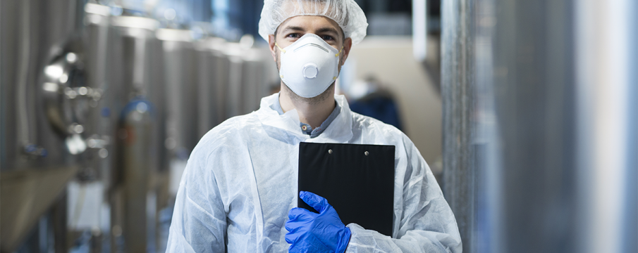 man wearing PPE mask, headcap, and gloves in a factory setting