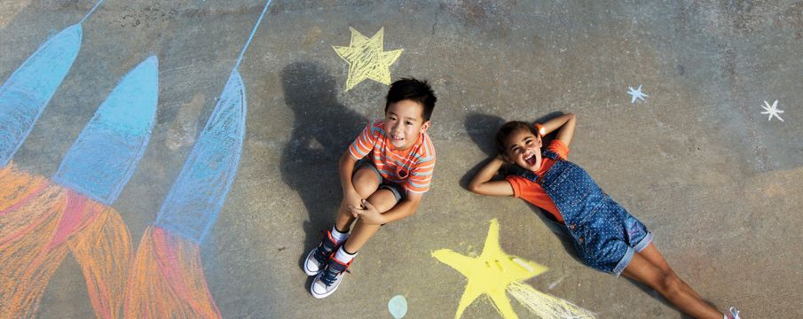 two kids laying on the pavement with chalk drawings around them