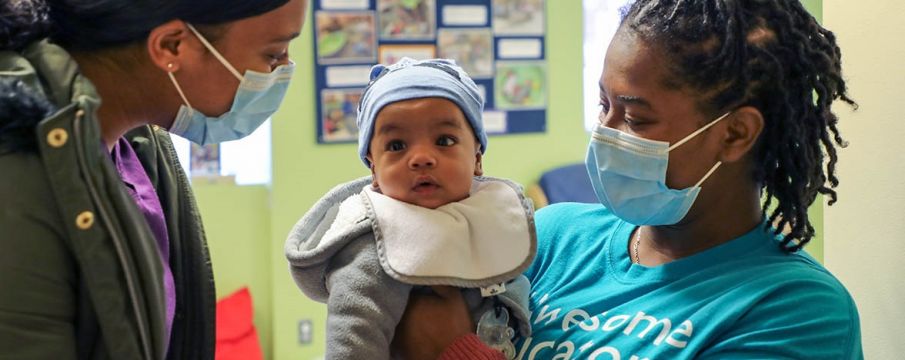 child care professional wearing a mask holding a baby