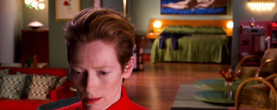 tilda swinton close up to the camera with a living room setting in the background