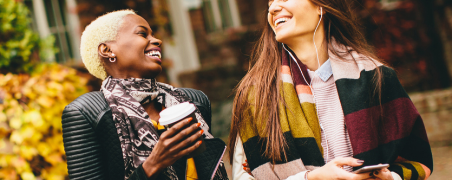 two women laugh and walk with a cup of coffee in stylish fall outfits