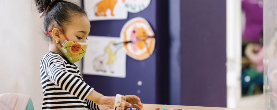 young girl doing crafts at a table wearing a face mask 