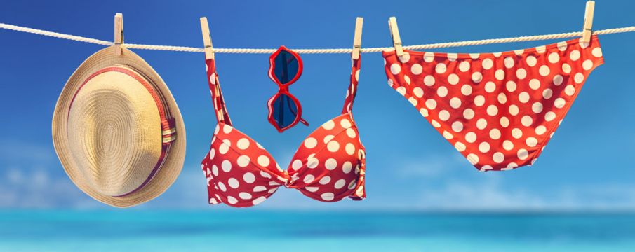 red bikini hangs on a clothesline with sunglasses and a straw sun hat at the beach