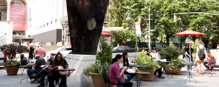 people sit at the tables and chairs provided by the LSBID around the movado clock in dante park