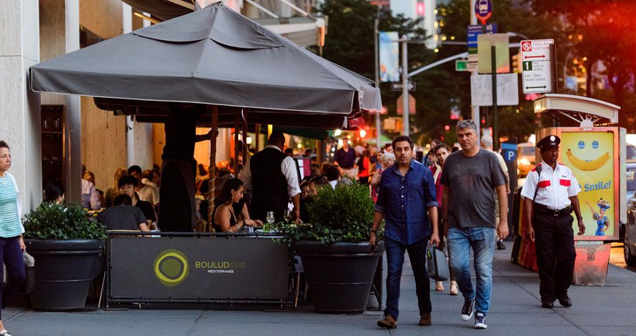 The outdoor seating area of a local restaurant on a summer evening as many pedestrians pass by